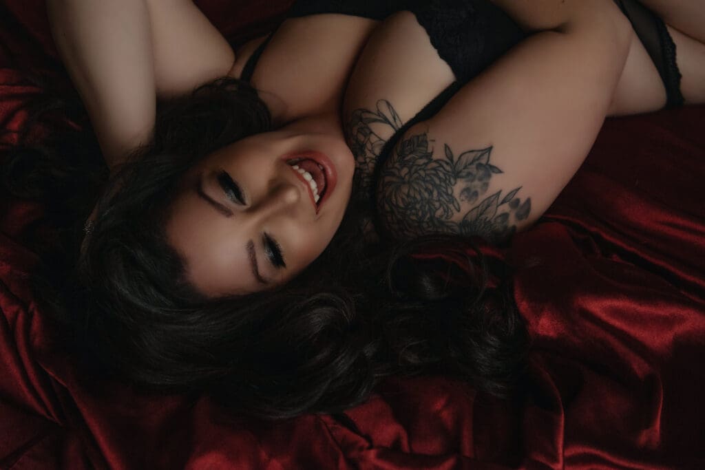 woman laying on bed with red satin sheets smiling in a bra