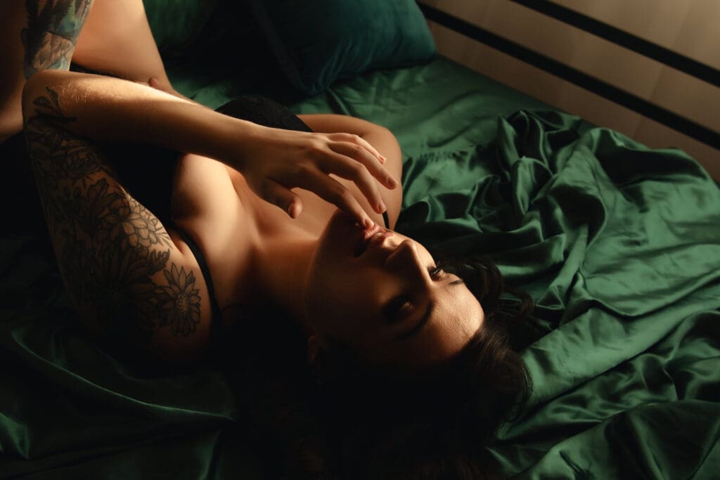 woman laying on her back on a bed with silk green sheets | Oculus Portraits