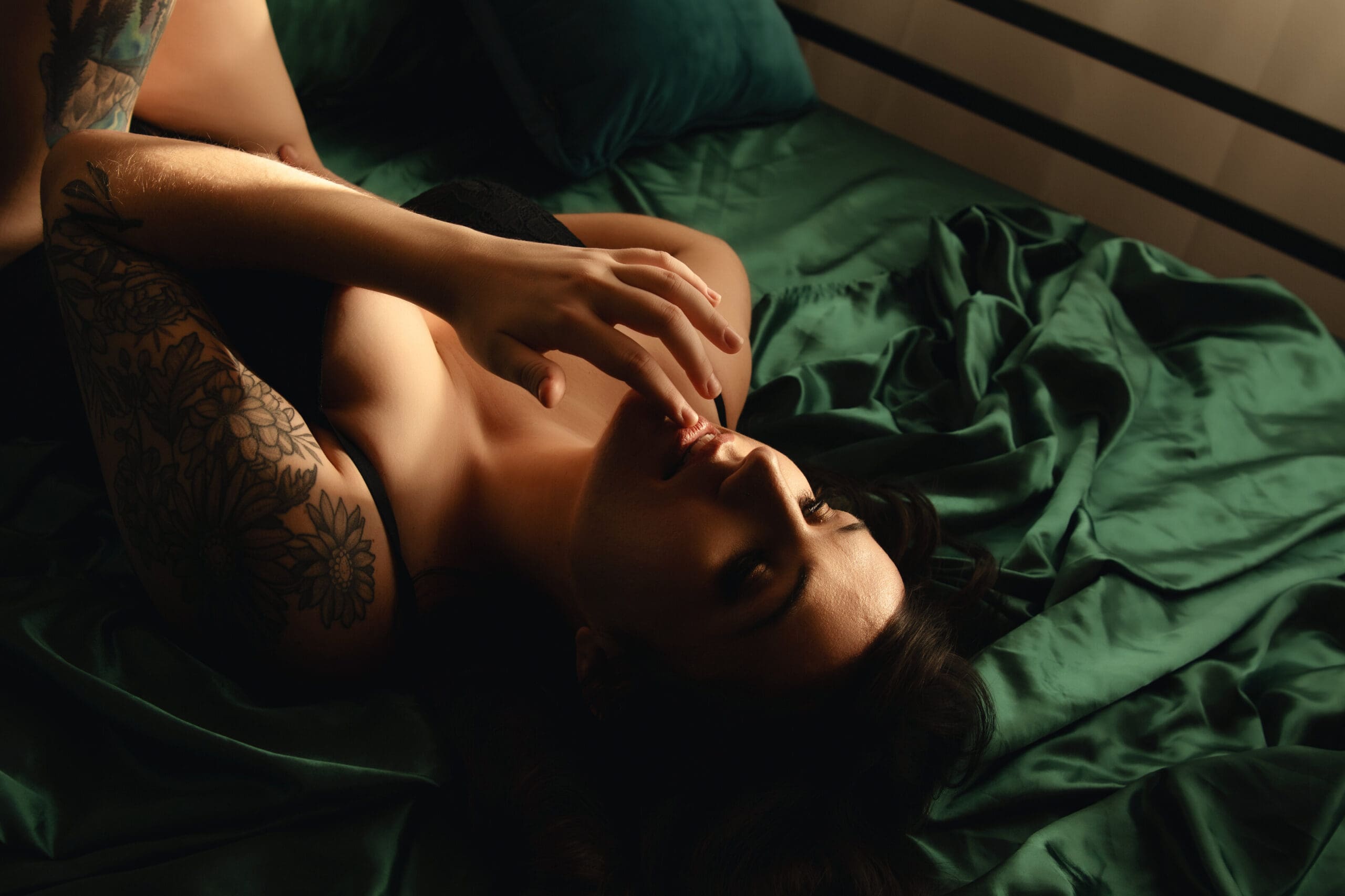 woman laying on her back on a bed with silk green sheets | Oculus Portraits